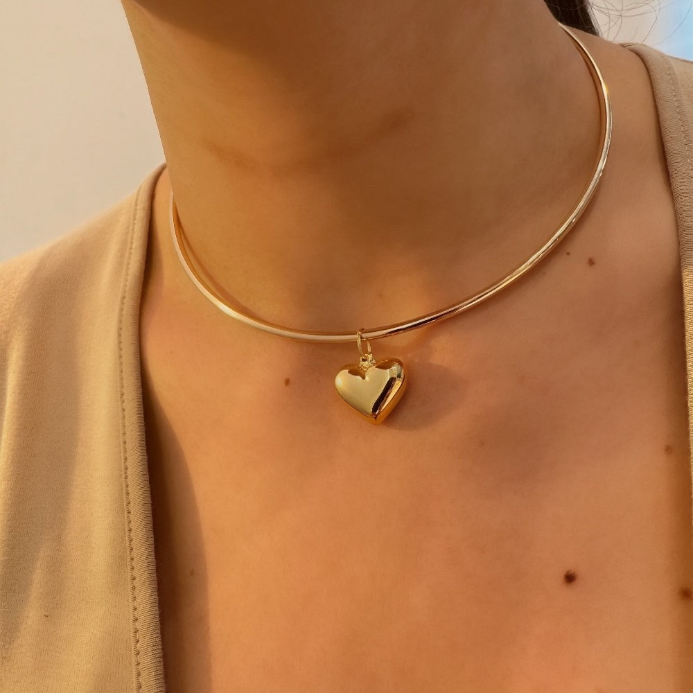 Gold necklace with a heart pendant worn by a person, with a blurred background.