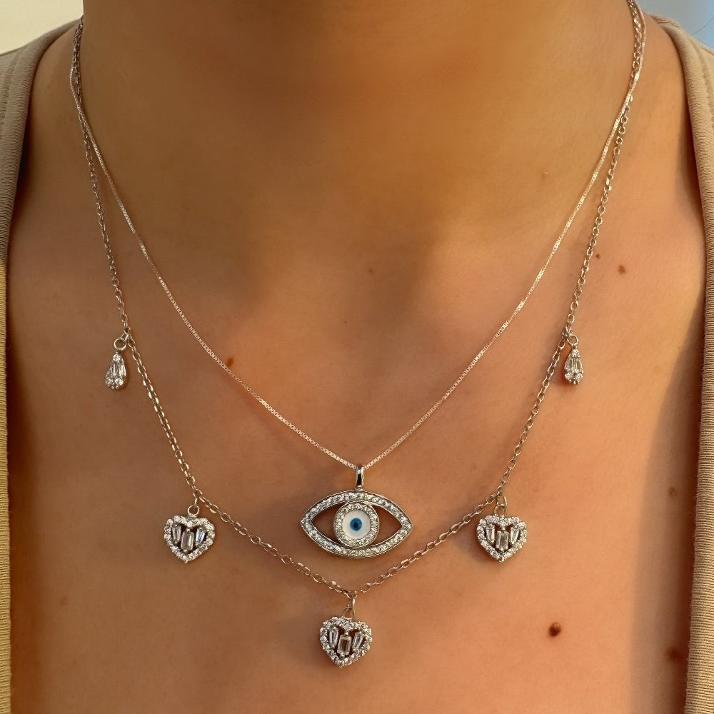 Necklace with eye pendant and heart-shaped charms on a person wearing a beige top.