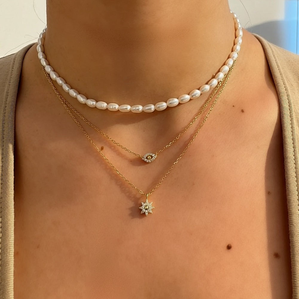 Person wearing a pearl necklace and a gold necklace with a pendant.