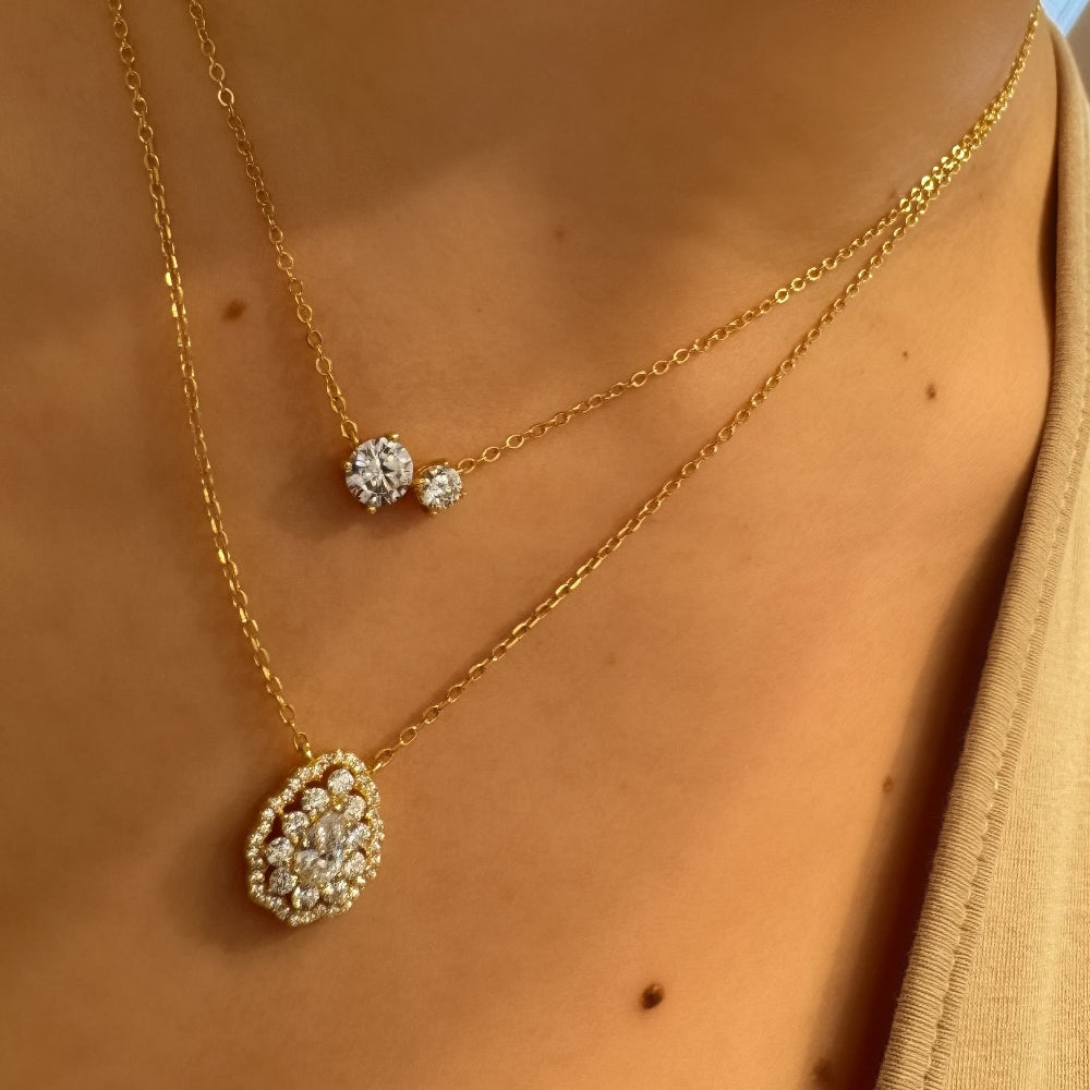 Gold necklace with a pendant on a person wearing a beige top.