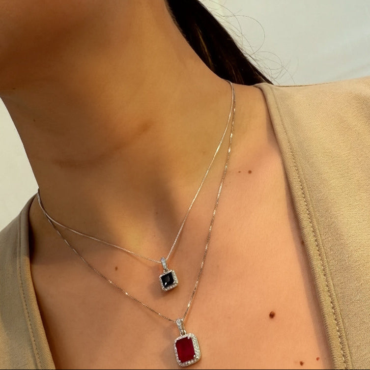 Person wearing a necklace with a red pendant and earrings.