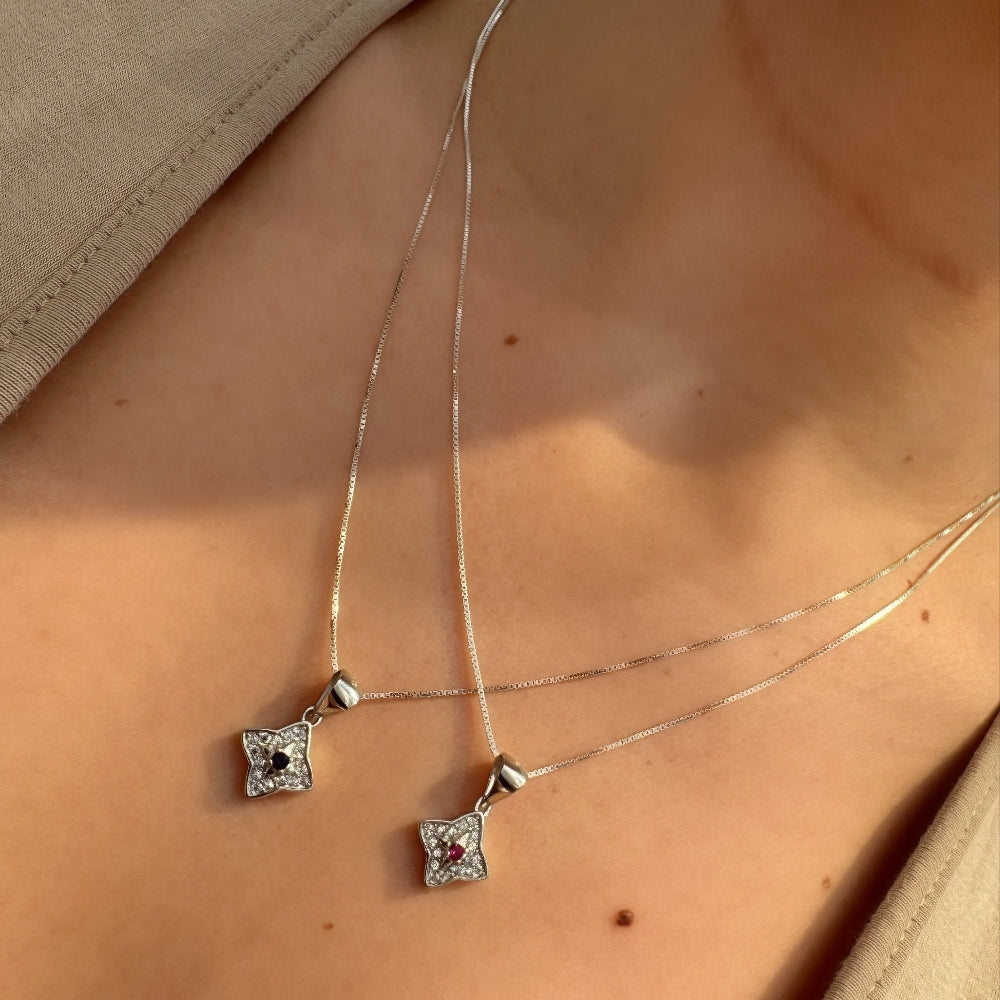 Silver necklace with square pendant on a person wearing a beige top.
