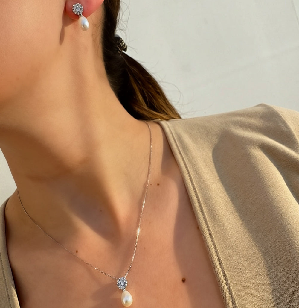 Close-up of a person wearing pearl earrings and a necklace with a pearl pendant.
