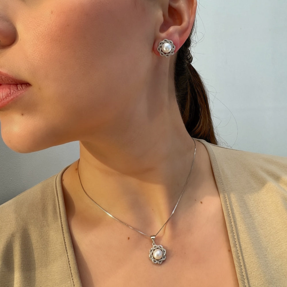 Close-up of a woman wearing pearl earrings and a necklace with a neutral background