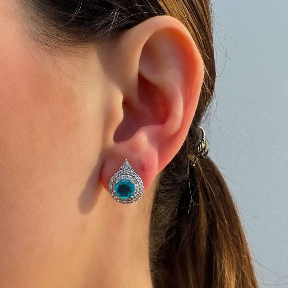 Close-up of a person wearing a turquoise earring with a silver setting against a light background