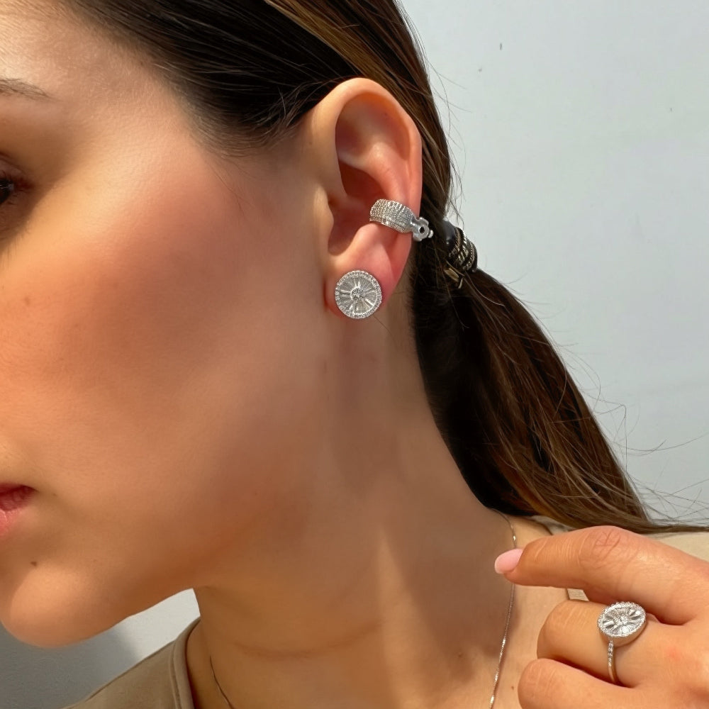 Close-up of a person wearing silver earrings and a ring, with a neutral background.