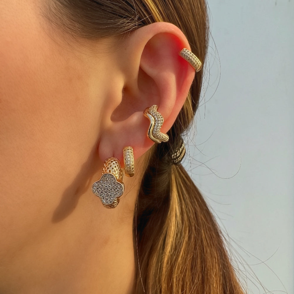 Close-up of a person's ear wearing gold hoop earrings with clear stones.