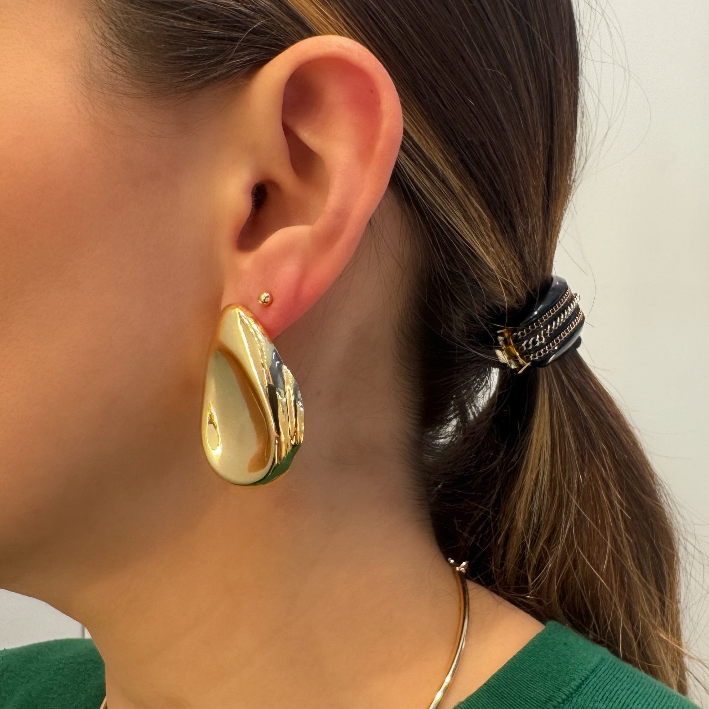 Close-up of a person wearing gold hoop earrings and a green top.