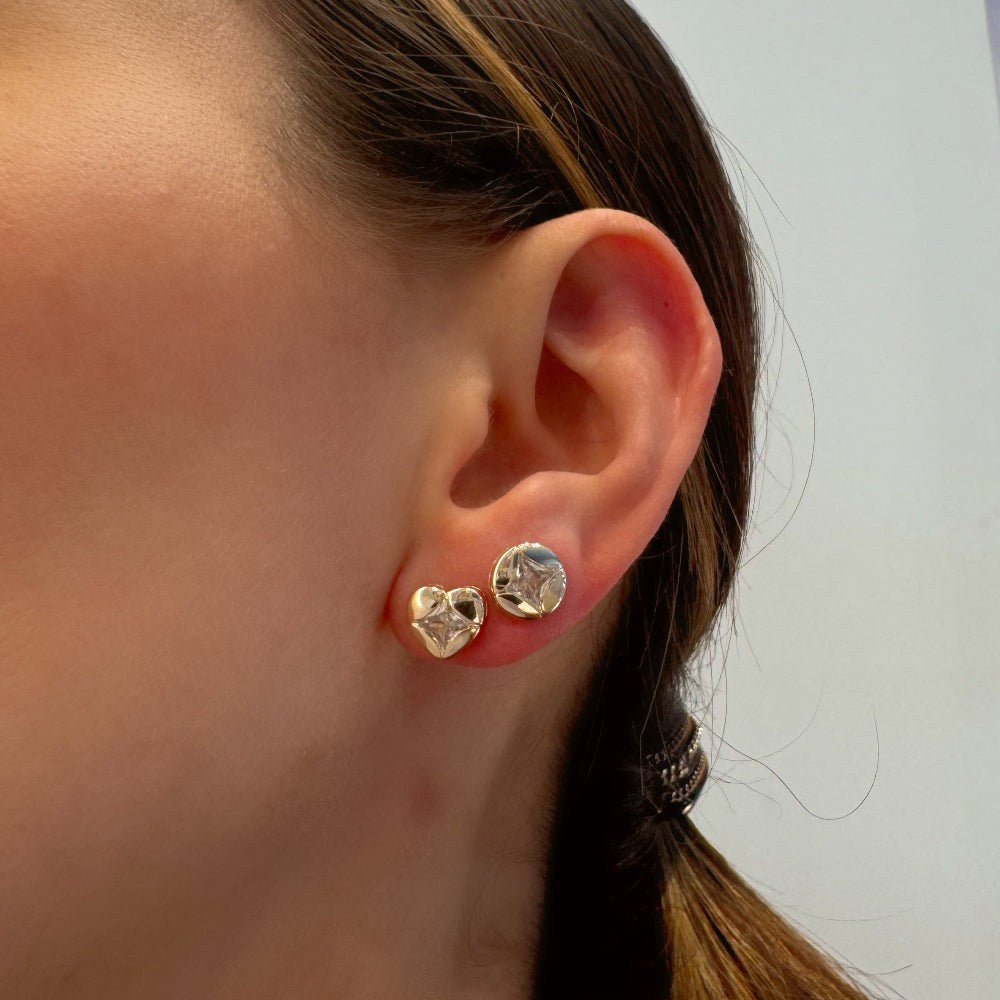 Close-up of a person wearing two heart-shaped earrings with a blurred background