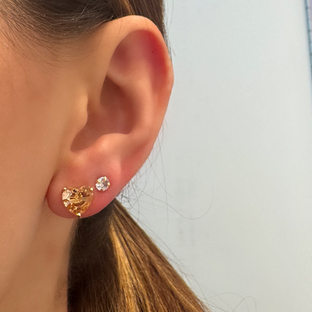 Close-up of an ear wearing gold earrings with a blurred background of jewelry display.