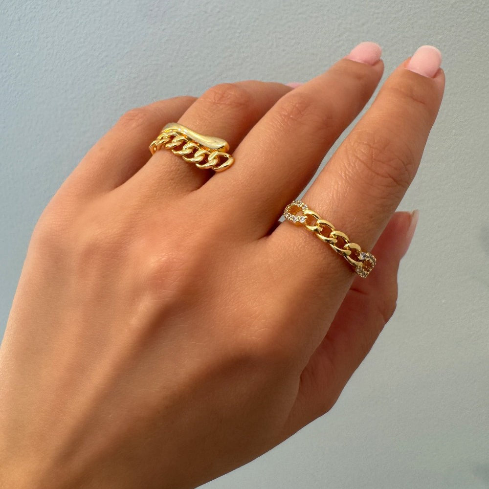 Hand wearing two gold chain rings on a light gray background