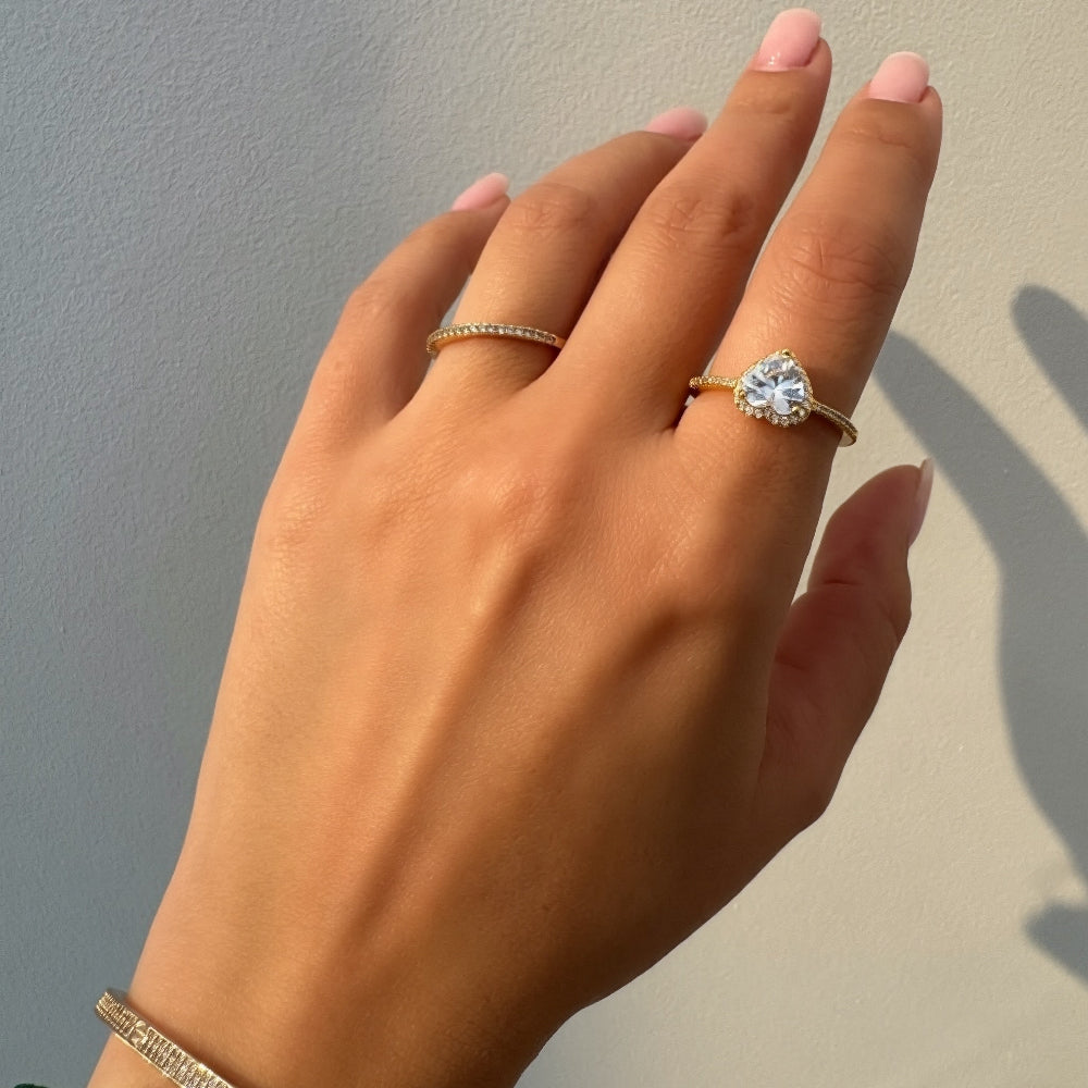 Hand wearing a gold ring and watch against a neutral background