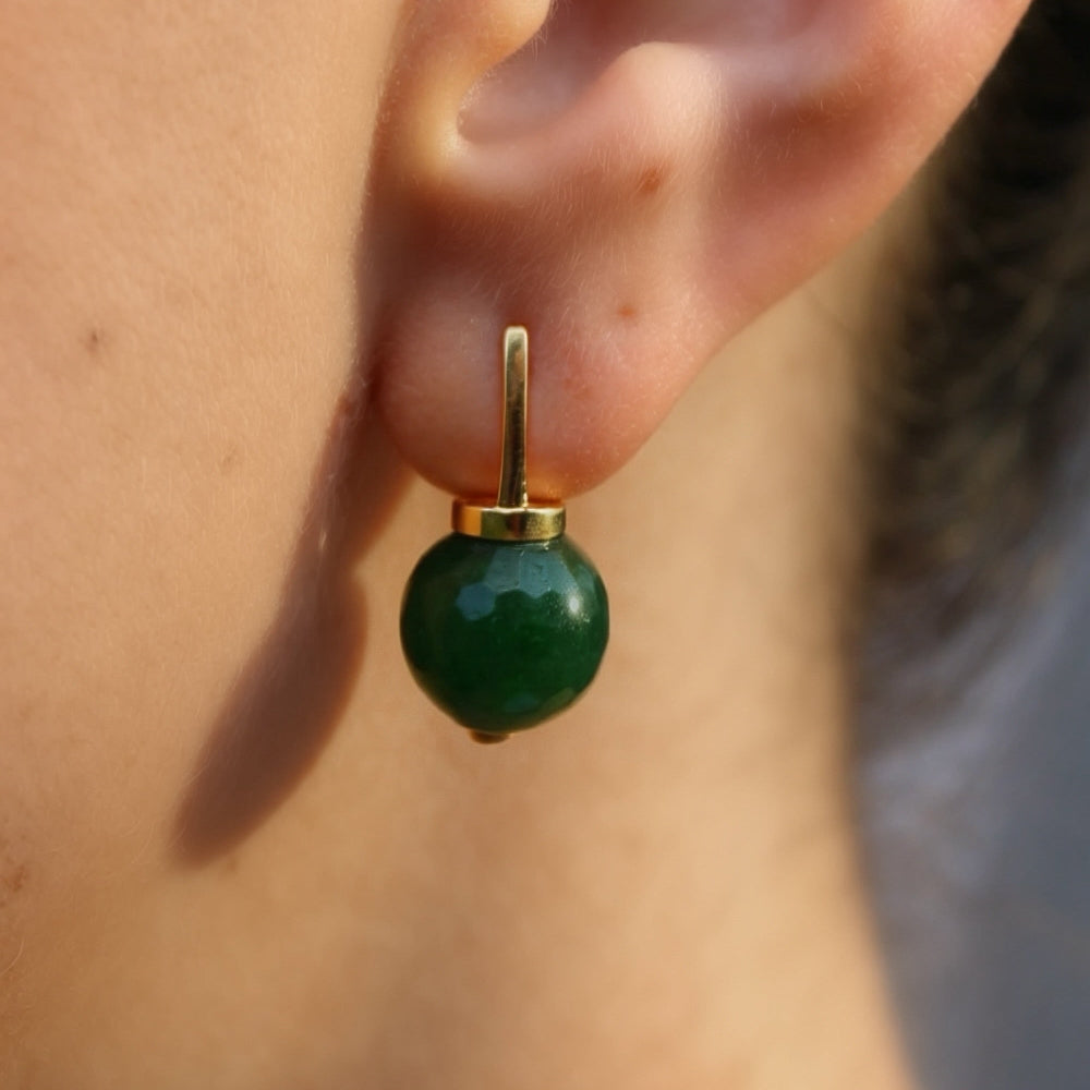 A close-up of a person's ear wearing a small gold hoop earring with a polished green bead drop.