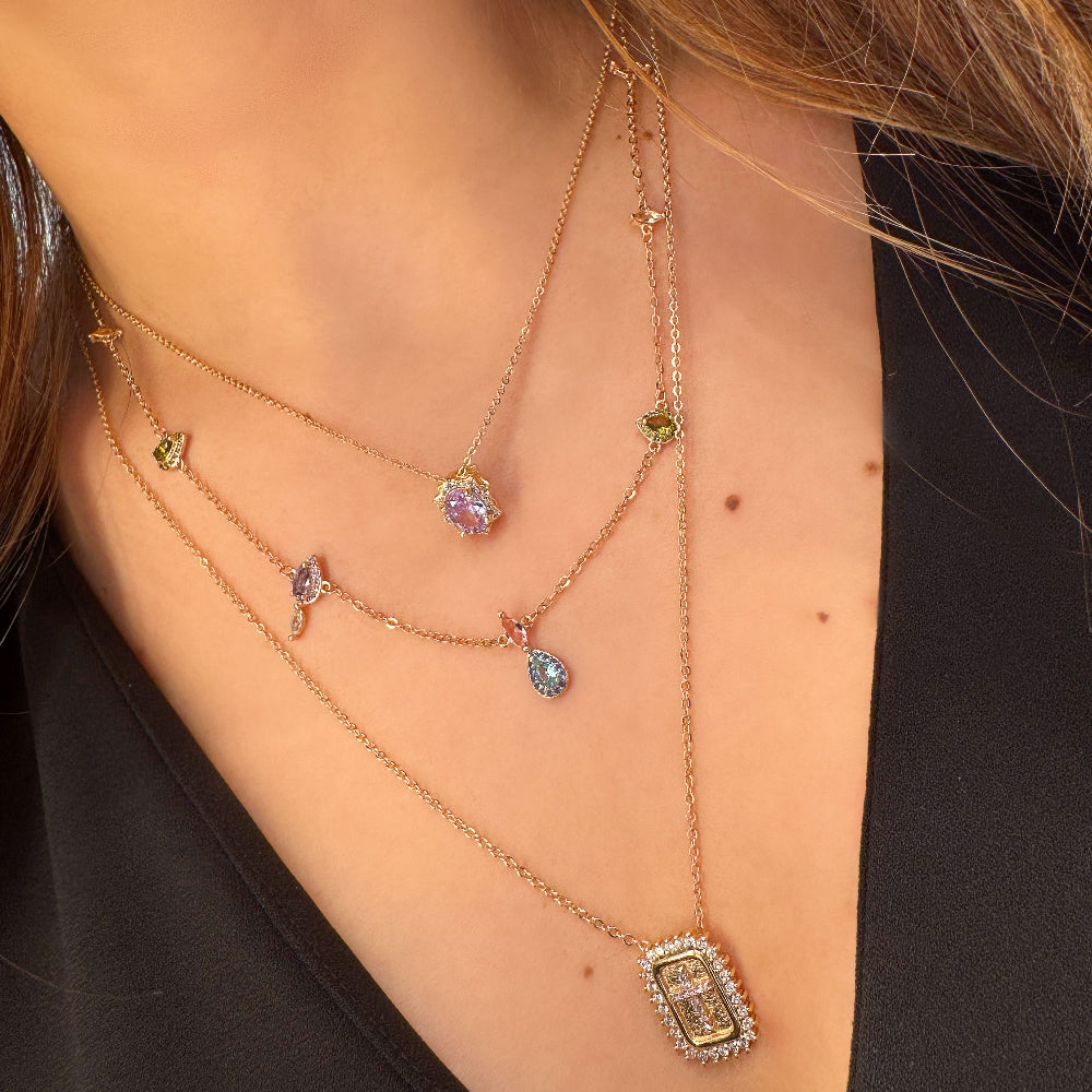 Close-up of a woman wearing multiple necklaces with gemstones on a plain background