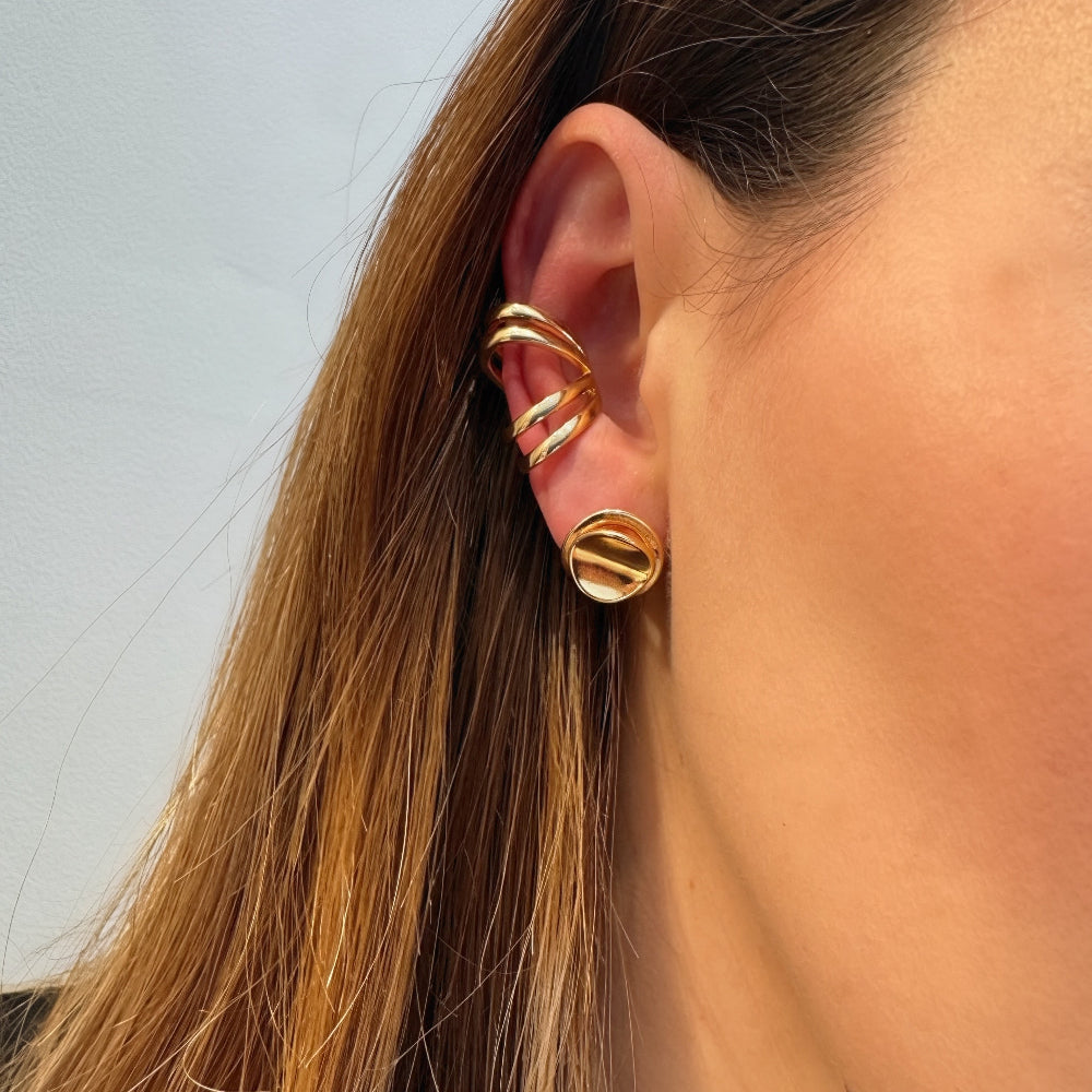 Close-up of a person wearing gold hoop earrings with a light blue background