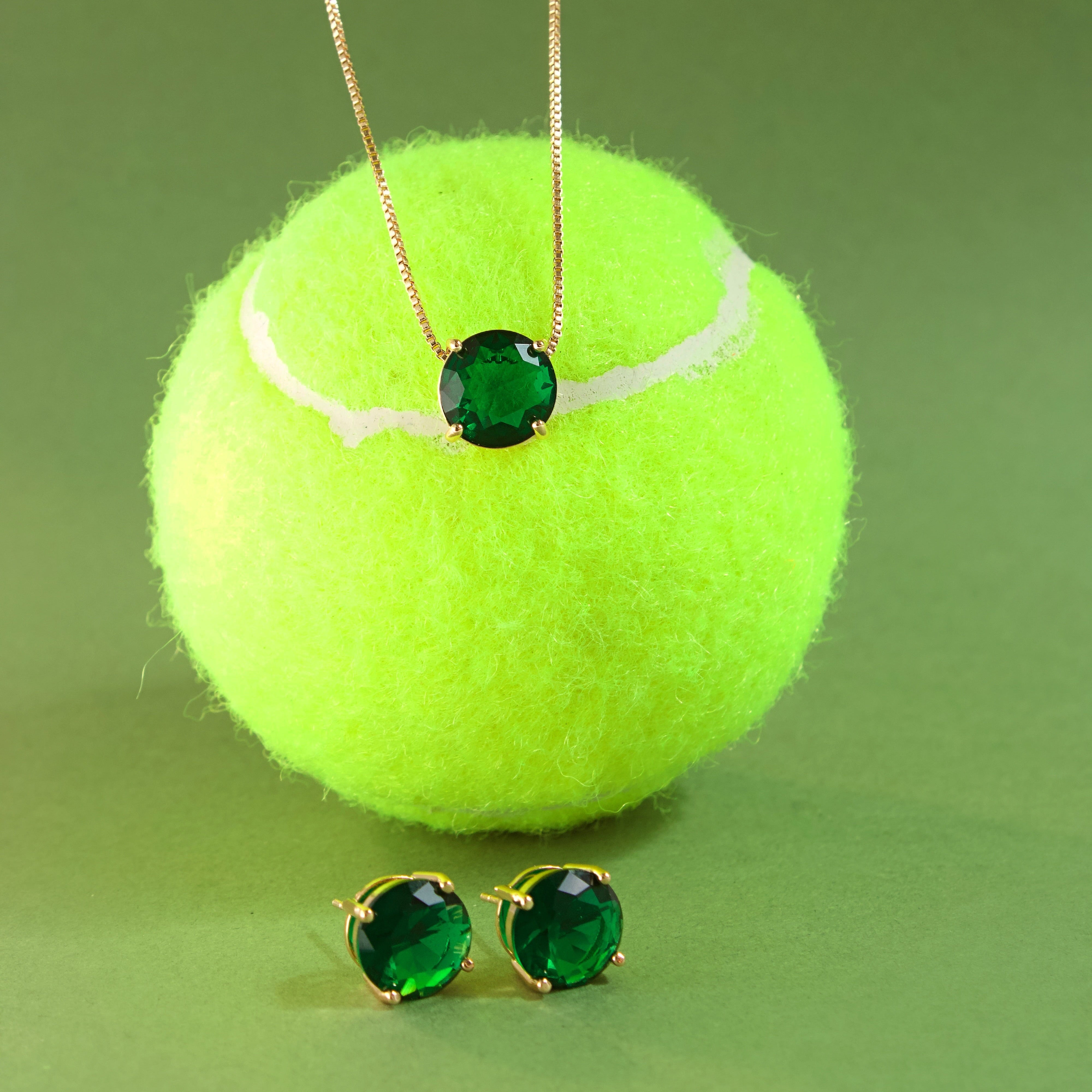 Tennis ball solitary emerald necklace and earrings on a green background