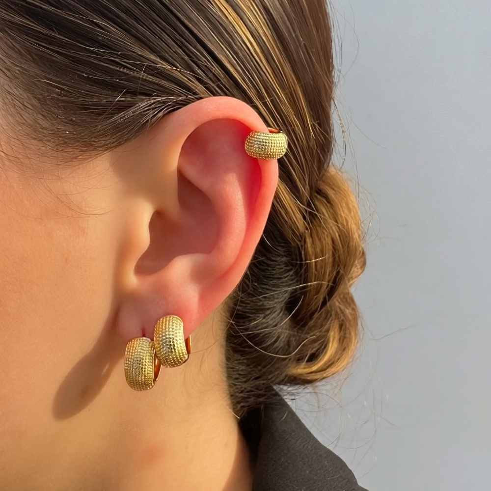 Gold hoop earrings worn by a person with a neutral background