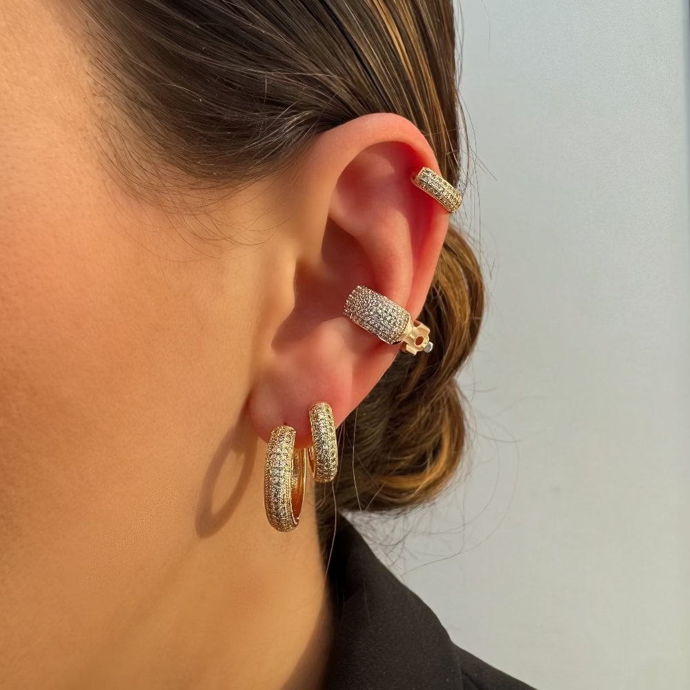 Close-up of a person's ear wearing gold hoop earrings with a plain background