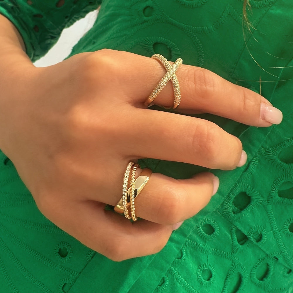Close-up of a hand wearing two gold rings on a green textured background