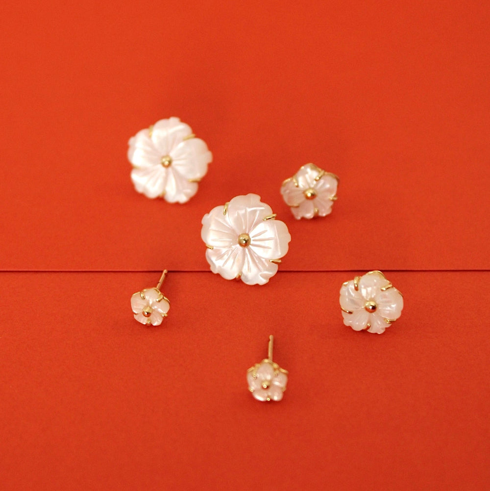Five white flower-shaped stud earrings with gold-tone settings arranged on a solid red background.