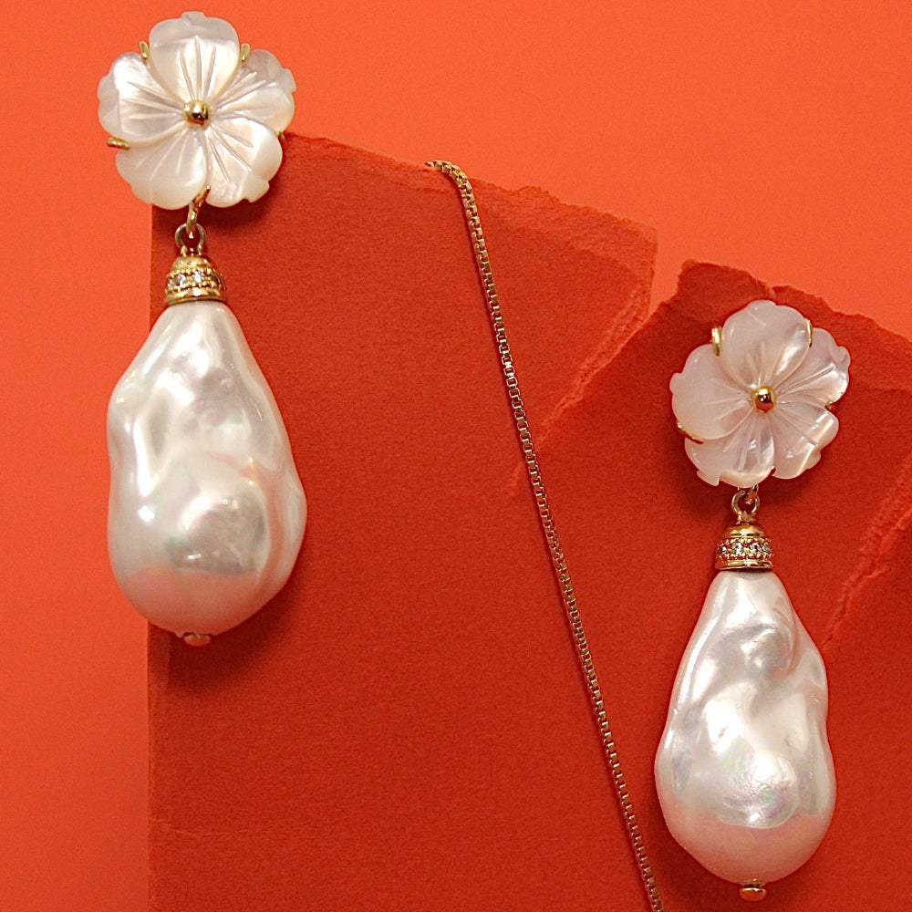 A pair of pearl baroque drop earrings with mother of pearls flower-shaped studs, displayed on a textured orange-red background.
