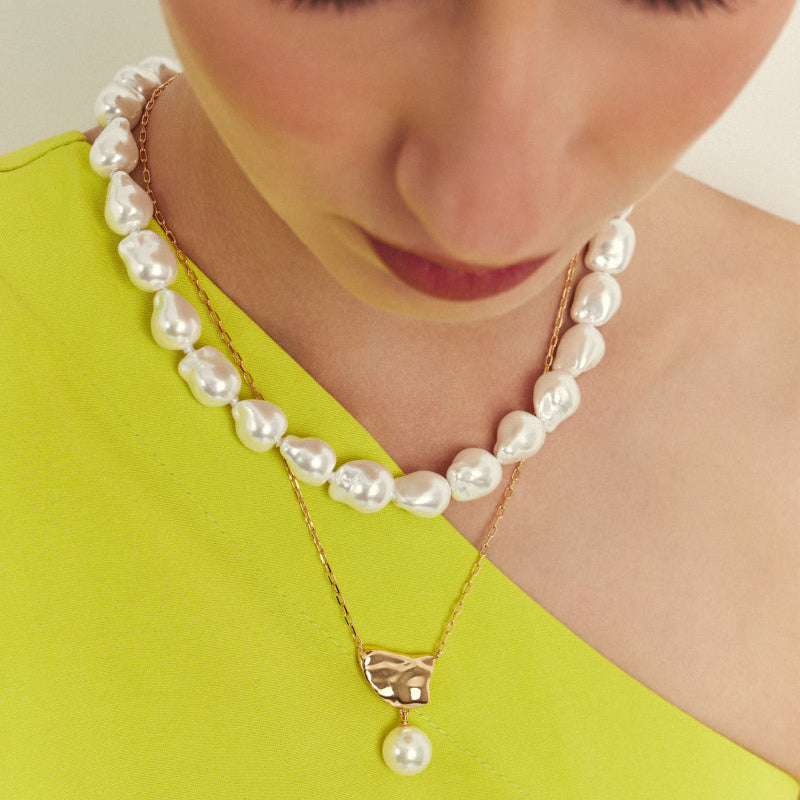Woman wearing a pearl necklace and earrings against a plain background
