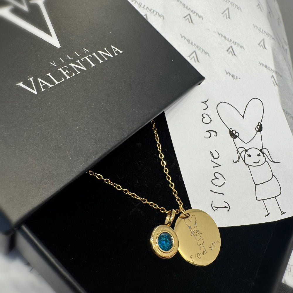 Gold necklace with a blue pendant on a Villa Valentina branded box.