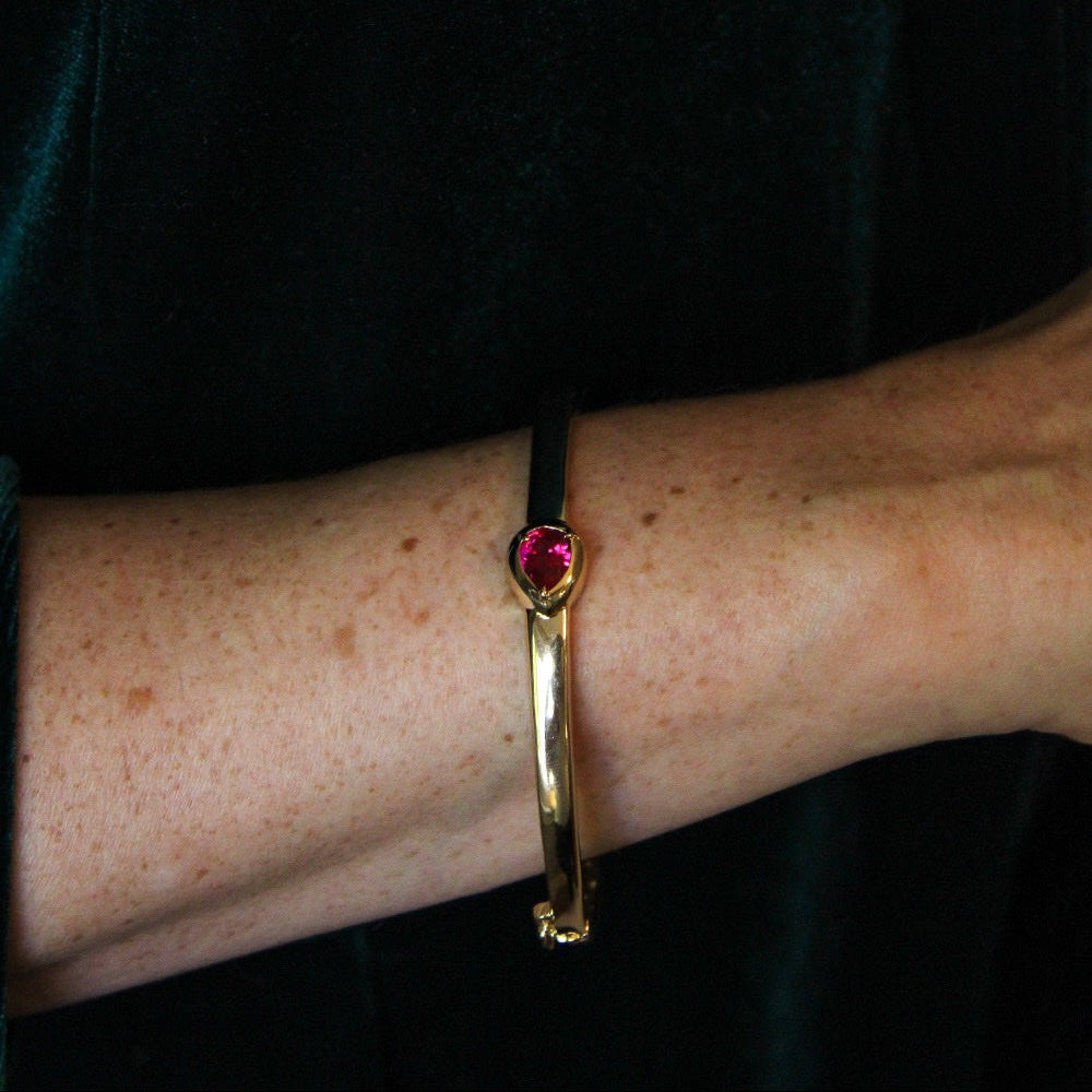 A gold bangle with a drop ruby July birthstone 