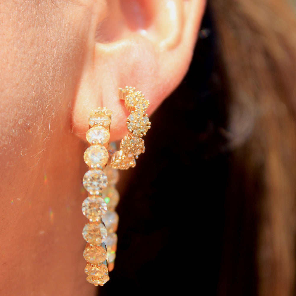 Close-up of a person wearing gold hoop earrings with clear stones.