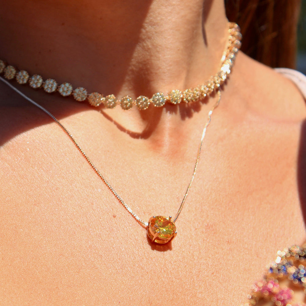 Close-up of a person wearing a necklace with a large yellow gemstone and a beaded choker.