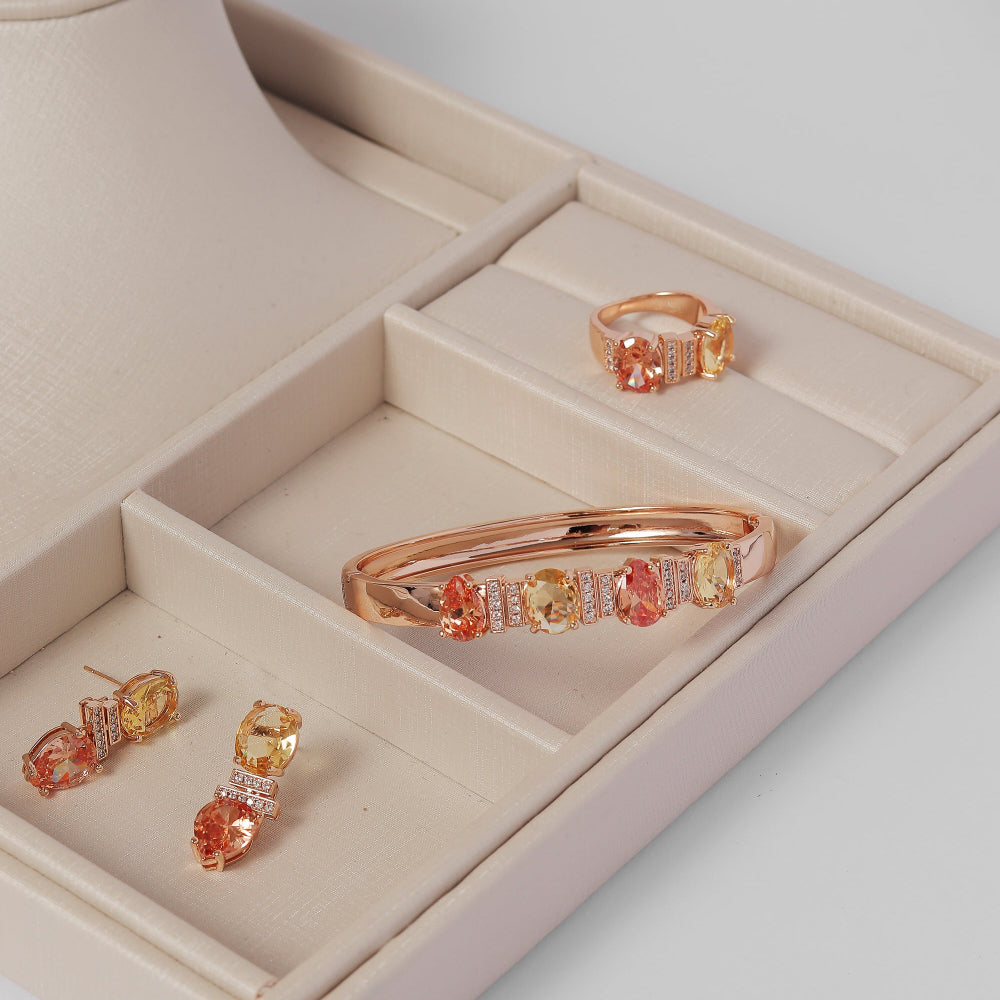 Jewelry set including a bracelet, ring, and earrings in a beige jewelry box on a light gray background.