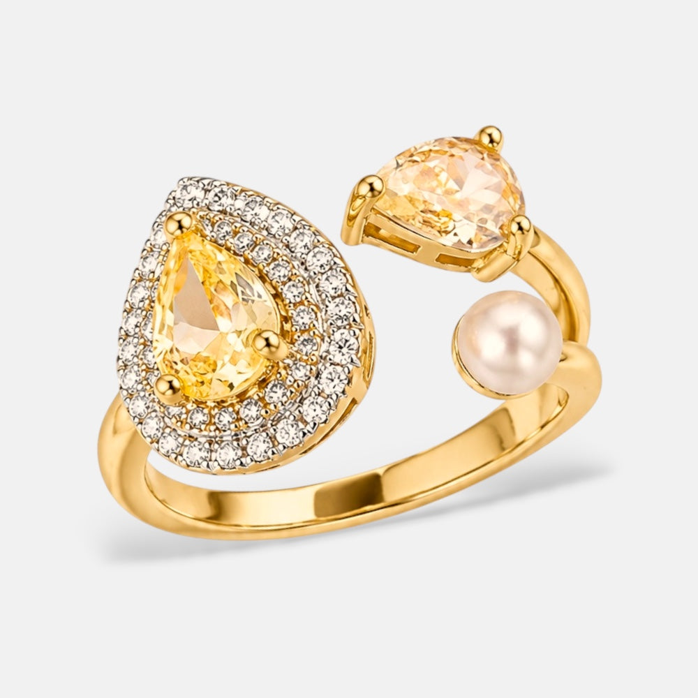 A gold ring featuring a large pear-cut yellow gemstone surrounded by a halo of small clear stones, with a smaller pear-cut pale pink gemstone and a round pearl on the band, set against a light gray background.