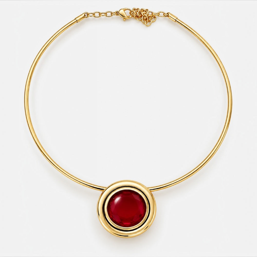 A gold bangle necklace featuring a prominent oval red gemstone pendant, displayed on a clean white background.