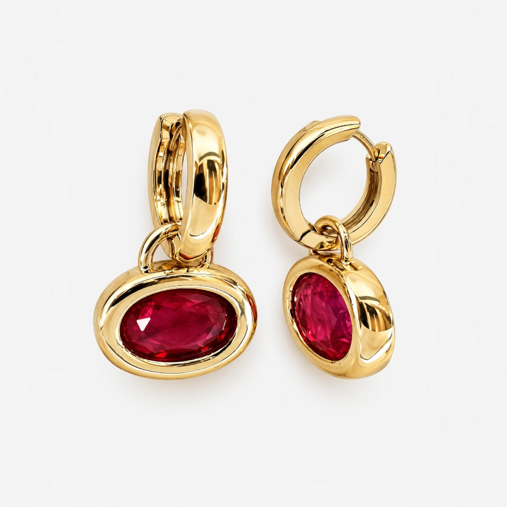 A pair of gold huggie hoop earrings with oval bezel-set deep pinkish-red gemstones, displayed on a clean white background.