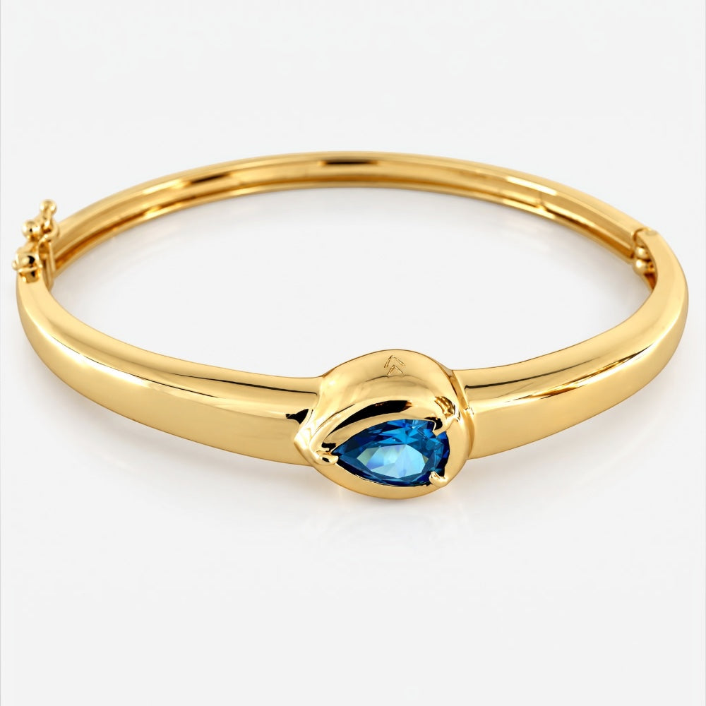 A polished yellow gold hinged bangle bracelet featuring a central marquise-cut blue gemstone, shown on a clean white background.