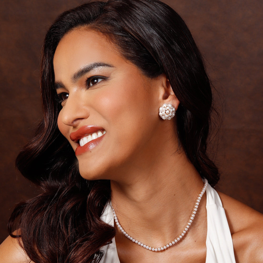 Woman wearing a pearl necklace and earrings against a brown background