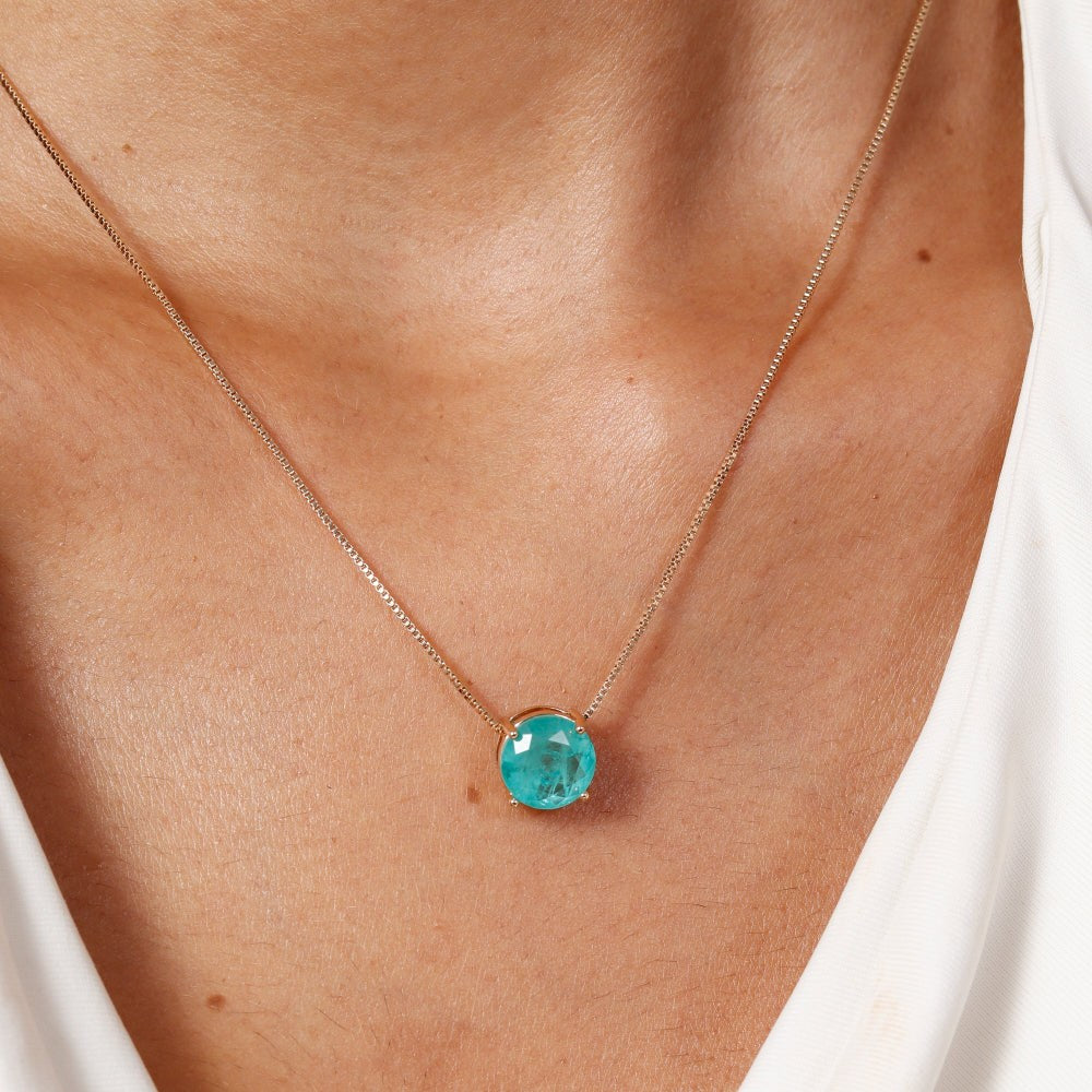 Necklace with a blue gemstone worn by a person against a white background