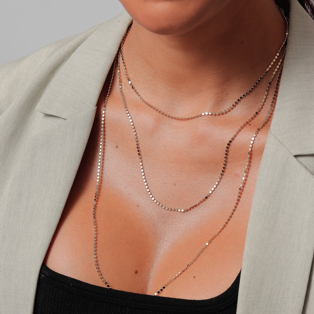 Close-up of a person wearing layered necklaces with a neutral background
