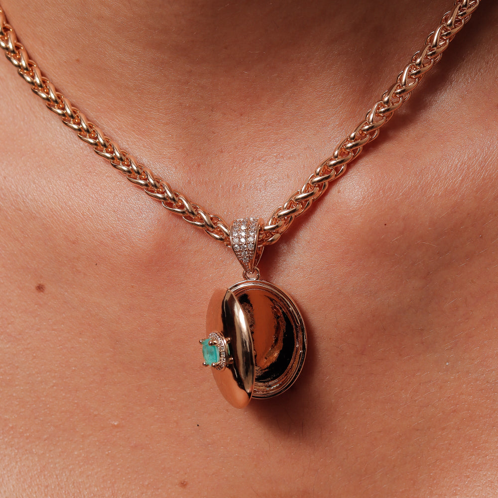 Rose gold necklace with a pendant featuring a green gemstone on a person's chest.