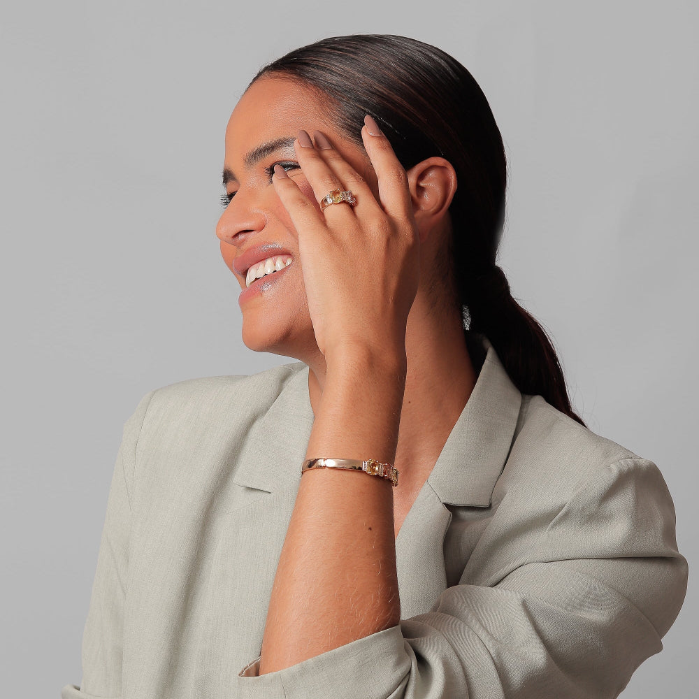 Woman wearing a light gray suit with jewelry against a plain background