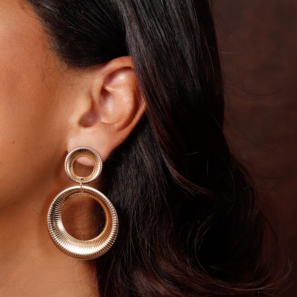 Close-up of a person wearing gold hoop earrings with a blurred background