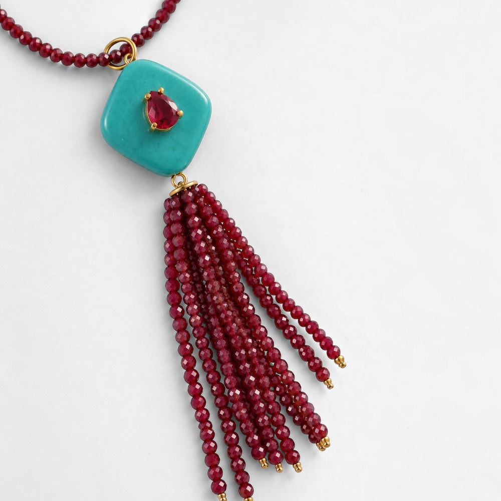 Close-up of coral-red jade bead necklace with reconstituted turquoise pendant and red beaded tassel