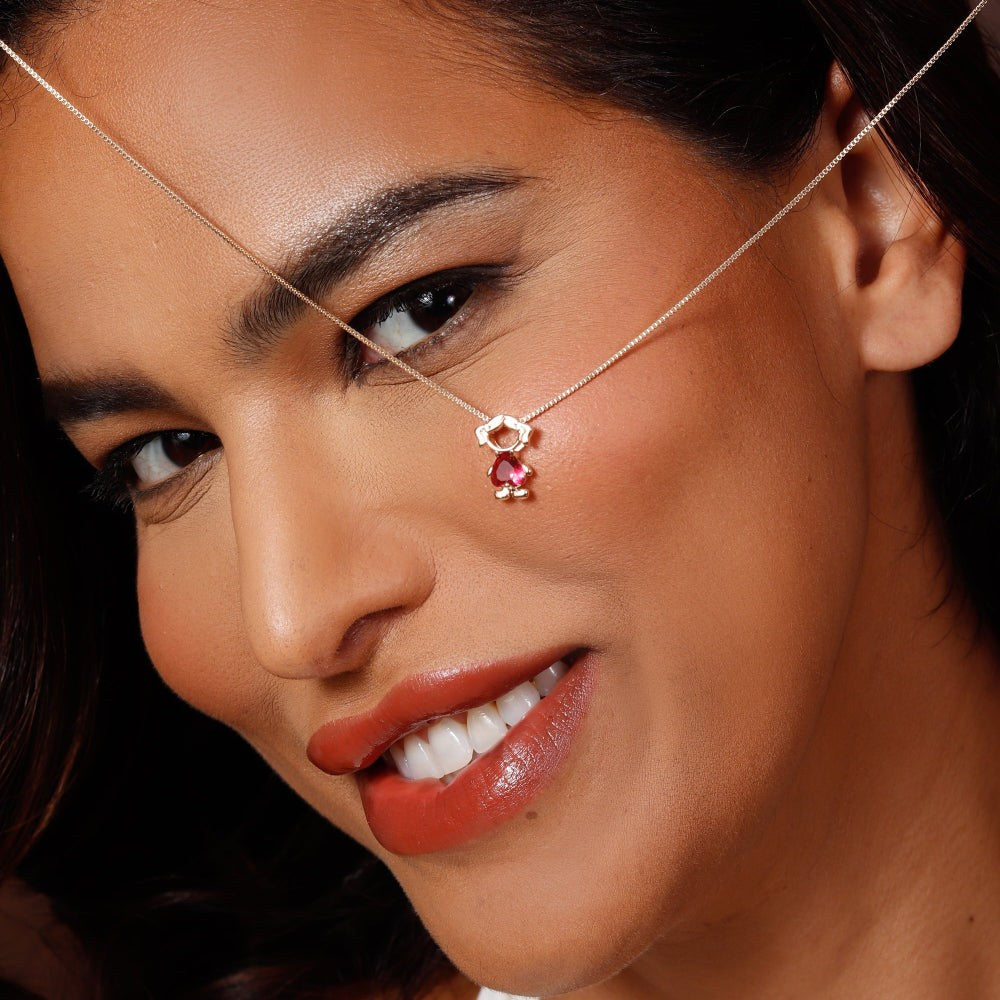 Close-up of a woman wearing a delicate necklace with a red gemstone.
